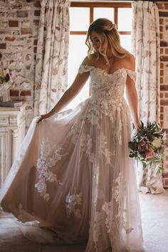 a woman in a wedding dress standing by a window