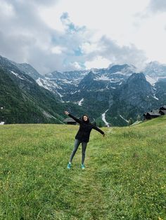 a woman standing on top of a lush green field next to mountains covered in snow