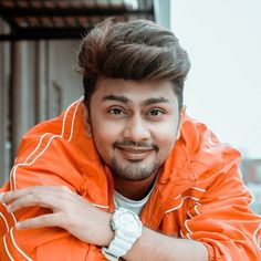 a man in an orange jacket posing for the camera with his hands on his chest