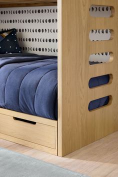 a wooden bunk bed with blue sheets and pillows on top of it, next to a gray rug