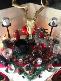 a table topped with candles and antlers on top of a red cloth covered table