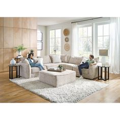 two people sitting on couches in a living room with wood floors and large windows