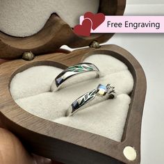 two wedding rings in a heart shaped wooden box with white and green designs on them