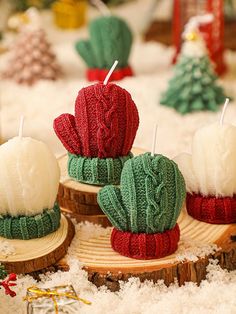 three knitted cactus candles sitting on top of wooden slices in the middle of snow