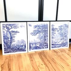 three blue and white paintings sitting on top of a hard wood floor next to a window