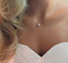 a woman wearing a white dress with a diamond necklace on her neck and hair in the wind