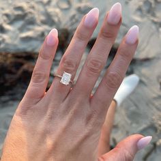 a woman's hand with a diamond ring on top of her left hand, next to the ocean