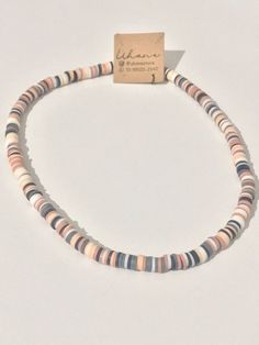 a necklace with multicolored beads is displayed on a white surface and has a tag attached to it