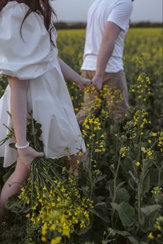 two people standing in a field with yellow flowers and one is holding the hand of another person