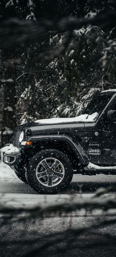 a black jeep parked on the side of a road covered in snow next to trees