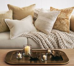 a tray with candles on top of it in front of a white couch and pillows