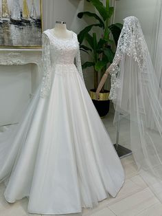 a wedding dress and veil on display in a room with a painting behind the mannequin