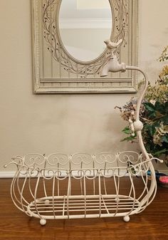 a white wire basket sitting on top of a hard wood floor next to a mirror