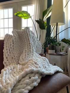 a large white blanket sitting on top of a brown couch next to a potted plant