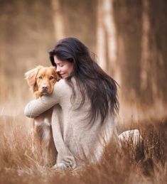 a woman sitting in the grass holding a dog with long hair and wearing a sweater