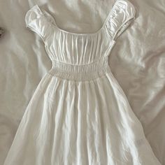 a white dress laying on top of a bed next to a pair of shoes and a purse