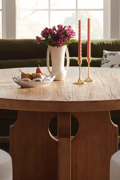 a wooden table topped with a white vase filled with flowers next to a candle holder