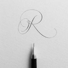 a pen writing the letter k on top of a piece of paper with ink in it