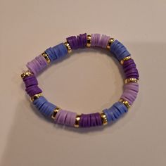 a purple and blue beaded bracelet on a white surface with gold beads in the middle