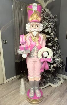 a pink and gold nutcracker statue in front of a christmas tree with presents