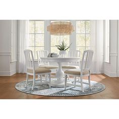 a white table with four chairs and a round rug in front of the window,