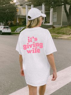 a woman is walking down the street wearing a white t - shirt that says it's giving wife