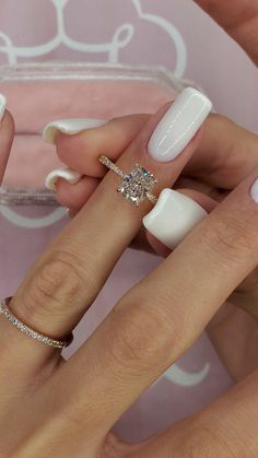 two hands with white manicures and rings on their fingers, one holding a diamond ring