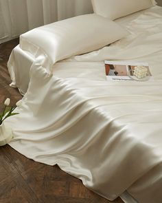 a bed with white sheets and pillows on top of it next to a flower vase