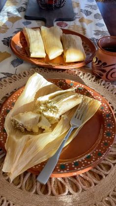 corn on the cob is sitting on an orange plate with a fork and knife