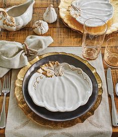 a place setting with white pumpkins and silverware on a wooden tablecloth, along with gold rimmed dishes