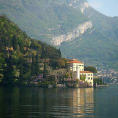 a house on the shore of a lake with mountains in the background