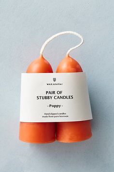 two orange candles sitting next to each other on a blue surface with a white tag that says pair of stubby candles