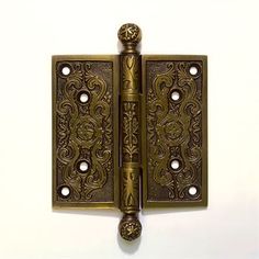 an antique brass door hinge with ornate designs on the front and back sides, set against a white background