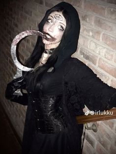 a woman dressed up as a nun holding a snake in her hand and wearing a black outfit