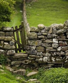 an old stone wall with a wooden gate in the middle and green grass around it