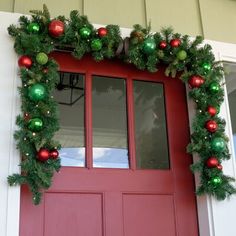 a red front door decorated for christmas with green and red ornaments