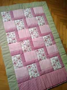 a pink and green patchwork quilt with polka dots on the bottom, sitting on a wooden floor