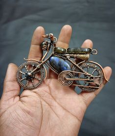 a hand holding a metal brooch with a bike on it