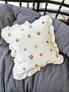 a white pillow with flowers on it sitting on top of a gray bedding set