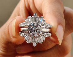 a close up of a person holding a ring with an engagement and wedding rings on it