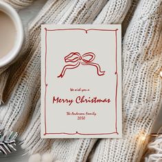 a white card with a red ribbon on it next to a cup of coffee and christmas decorations