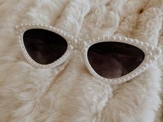 a pair of white sunglasses with pearls on the sides and black lenses are laying on a fur surface