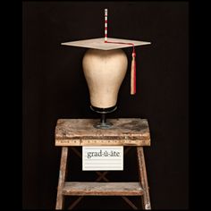 a graduation hat sitting on top of a wooden stool next to a sign that reads grad - ate