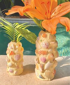 two vases with flowers and seashells on the outside near a swimming pool