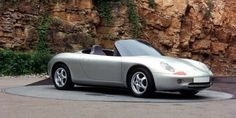 a silver sports car parked in front of a rock wall