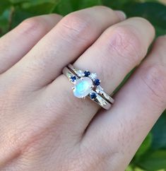 "A unique oval-shaped faceted rainbow moonstone engagement ring set accented with 2 petite genuine blue sapphires complemented with a matching contour wedding band featuring genuine blue and white sapphires handcrafted in sterling silver. Wrapped in a box ready for gift-giving.(r-egt-9) Instagram Video --------------- https://instagram.com/p/Bl3qWYXFgUA/ Can be custom made in any material and gemstones Center stone measure 7mm x 6mm Side Stone measures 2.2mm ----> Please note there is an addi Rainbow Moonstone Engagement Ring, Moonstone Engagement Ring Set, Sapphire Engagement Ring Set, Contour Wedding Band, Moonstone Engagement, Moonstone Engagement Ring, Sapphire Engagement Ring, Bridal Ring Set, Sapphire Engagement