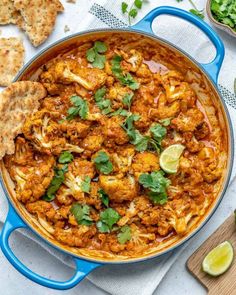 chicken curry in a blue pan with pita chips and cilantro on the side