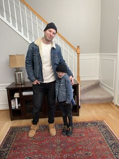 a man standing next to a little boy on top of a rug in front of a stair case