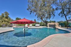 an outdoor swimming pool surrounded by trees and water features a large red umbrella over it