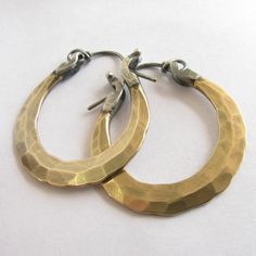 "Small handcrafted forged bronze hoops with sterling silver ear wires. Artfully hammered for dynamic texture and fitted with 20 gauge ( standard size) sterling silver ear wires with a secure and easy to use friction clasp. Lightweight at less than 4 grams each.A perfect pair for any time, anywhere! 1 and 1/8\" wide or 2.66cm and apx. 1.25\" tall or 3.1cm. If you would prefer a slighter thicker (18 gauge) ear wire please let us know in notes to seller at the time of purchase. The pair pictured ha Metalsmith Jewelry, Metalsmithing Jewelry, Mixed Metal Earrings, Hammered Hoop Earrings, Bronze Earrings, Hammered Earrings, Ear Gauges, Metal Earrings, Brass Earrings